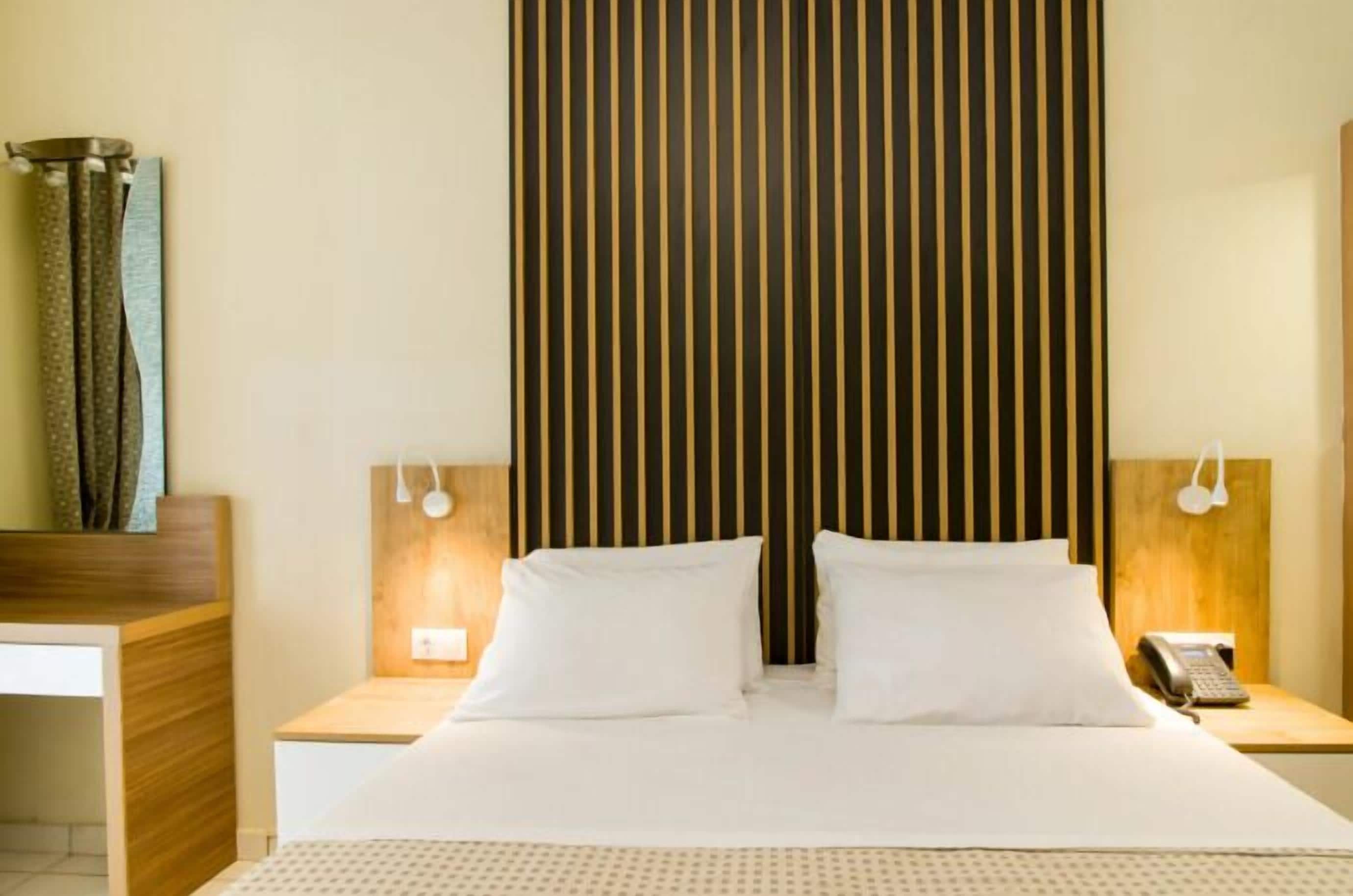 Habitación de hotel con una cama grande, dos mesitas de noche, un cabecero de madera y un teléfono sobre una de ellas.