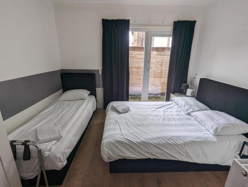 A hotel room with two beds, a window with curtains, and a view of the outside.