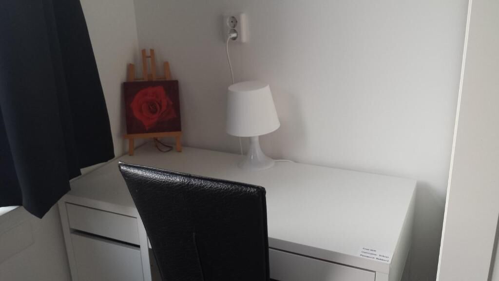 Una habitación pequeña y limpia con escritorio, silla, lámpara y un cuadro en la pared.