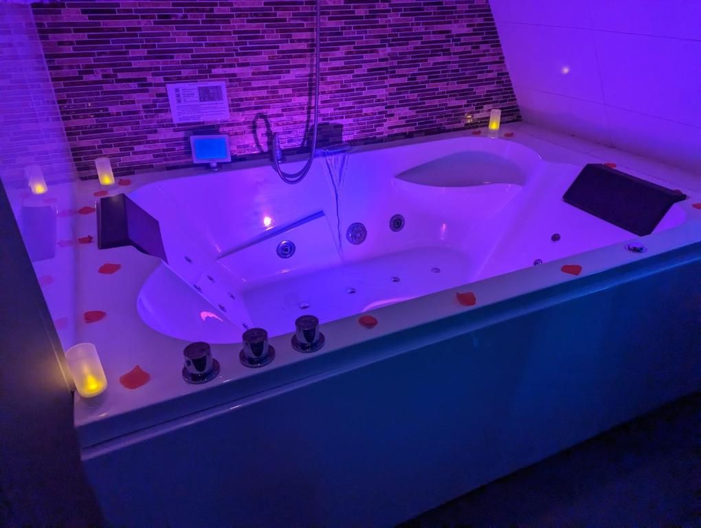 Un bain à remous agrémenté de pétales de rose, doté d’un panneau de commande et orné d’un mur aux motifs de briques.