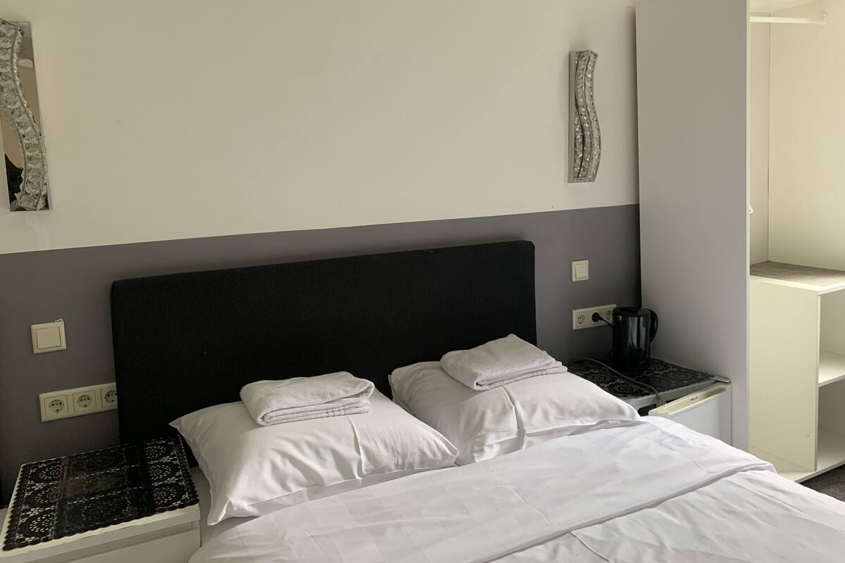 Un lit bien fait, avec du linge de lit blanc, une tête de lit noire et deux tables de chevet avec des lampes.