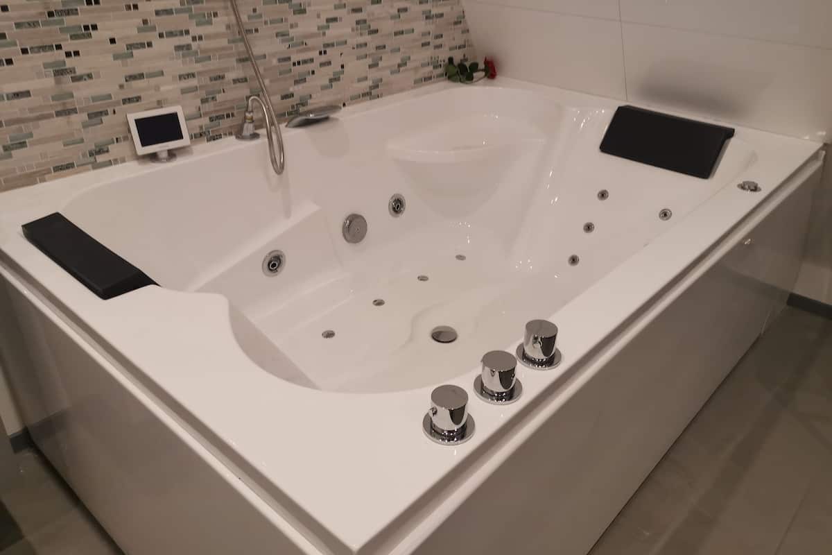Une salle de bain moderne avec une grande baignoire, une douchette à main et un petit écran fixé au mur.