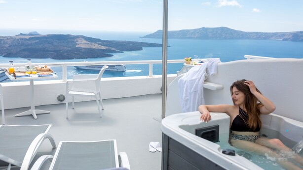 A balcony with a hot tub, white chairs, and a table with breakfast items. - Asma Suites (Santorini)