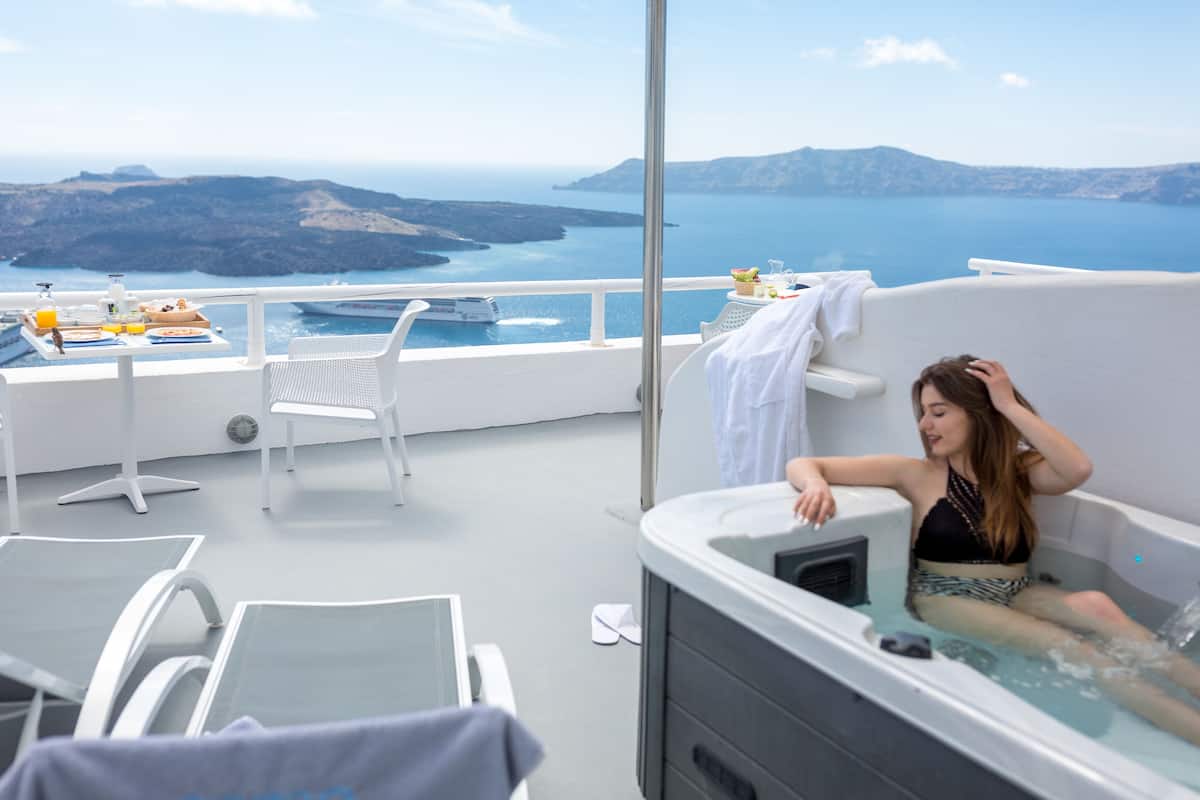 A balcony with a hot tub, white chairs, and a table with breakfast items.