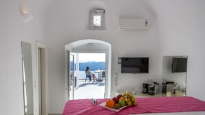 A hotel room with a bed, a fruit plate, a coffee maker, and a TV. - Asma Suites (Santorini)
