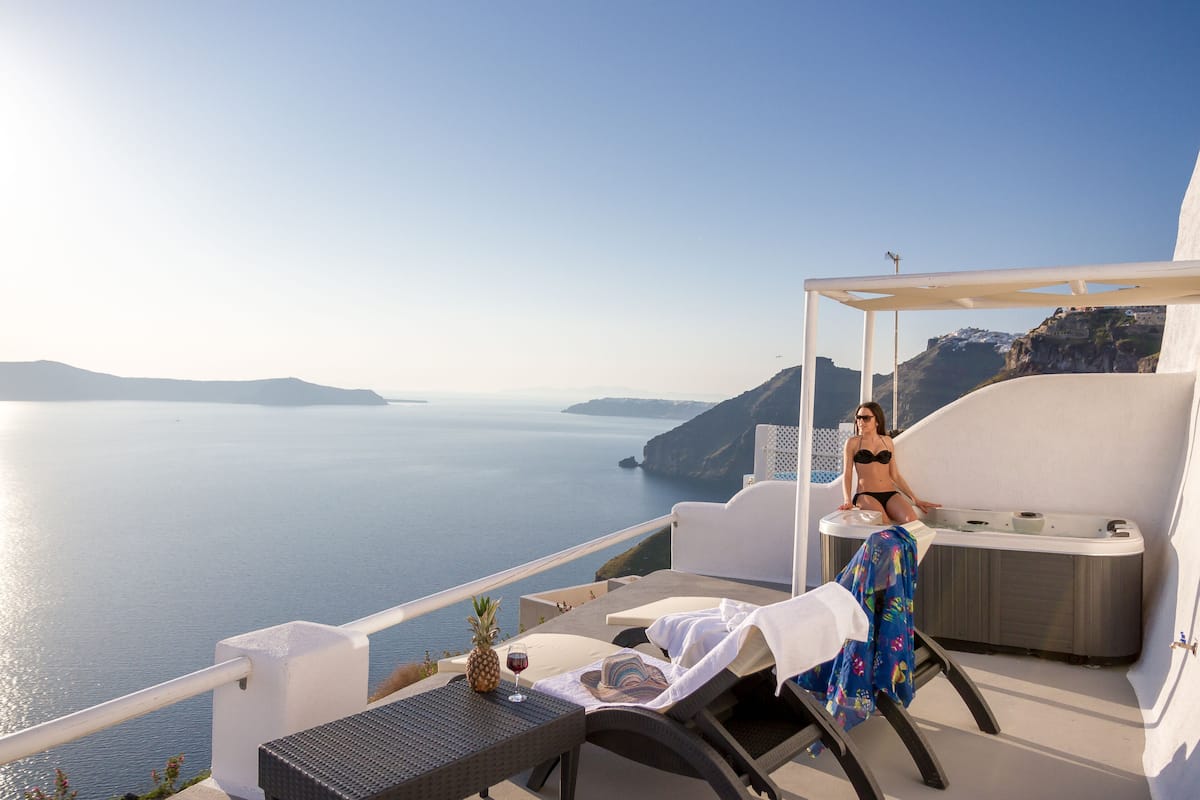 A balcony with a view of the sea, a hot tub, and a table with a pineapple and wine glass.