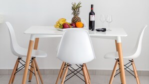 A white table with a fruit bowl, a bottle of wine, and two glasses. - Asma Suites (Santorini)