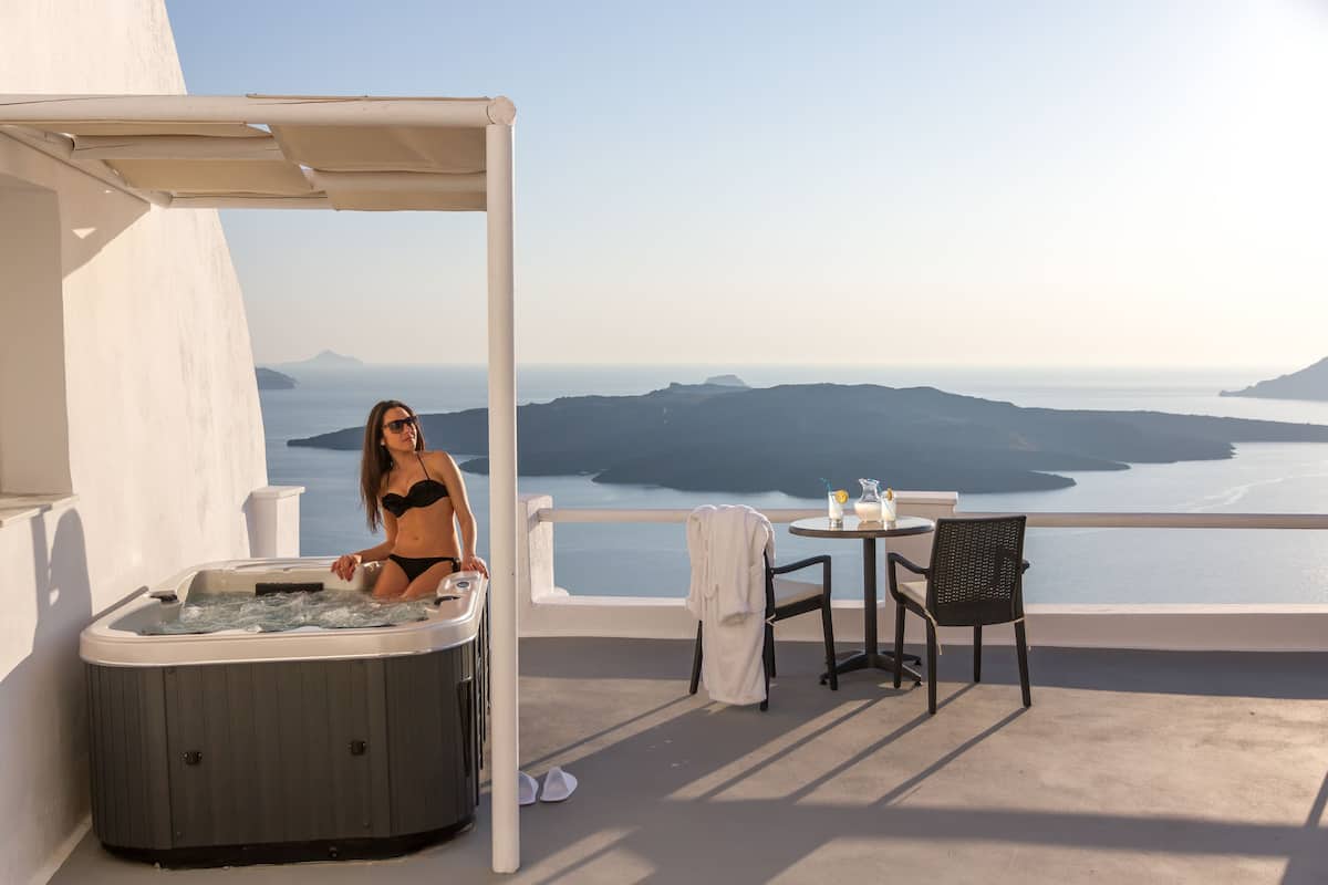 A balcony with a hot tub, a table with chairs, and a view of the sea and mountains.