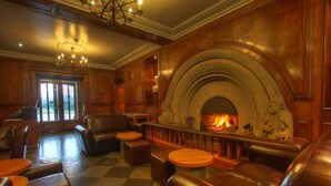 A cozy lounge area with leather sofas and round tables, a fireplace, and a checkered floor.