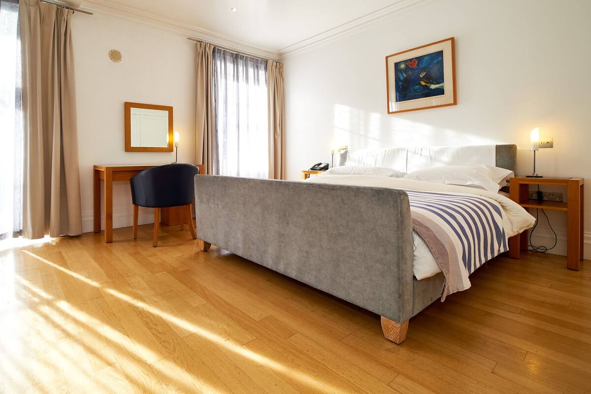 Hotellihuone, jossa on suuri sänky, työpöytä, tuoli ja yöpöytä, jossa on lamppu.