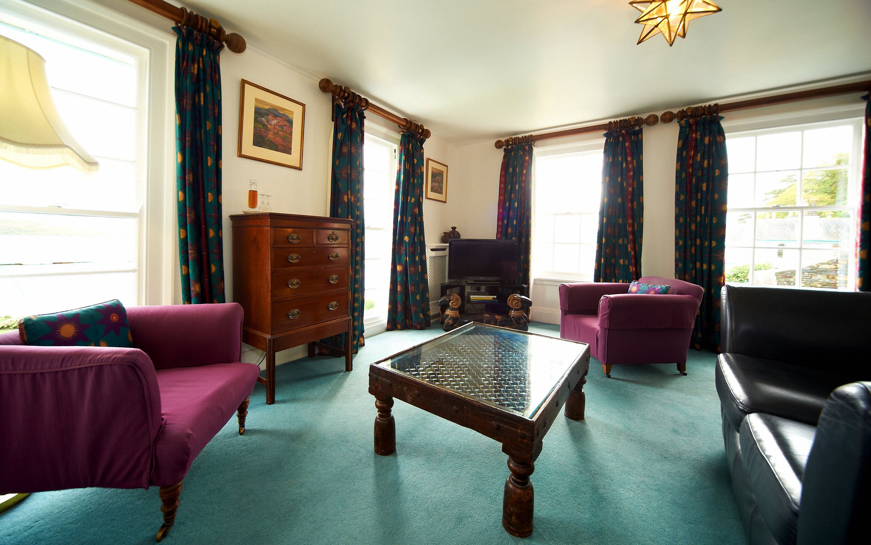 A living room with a wooden coffee table, purple armchairs, a black leather sofa, a wooden cabinet, and a television.