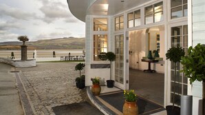 A hotel entrance with a stone-paved walkway, potted plants, and a view of the landscape.