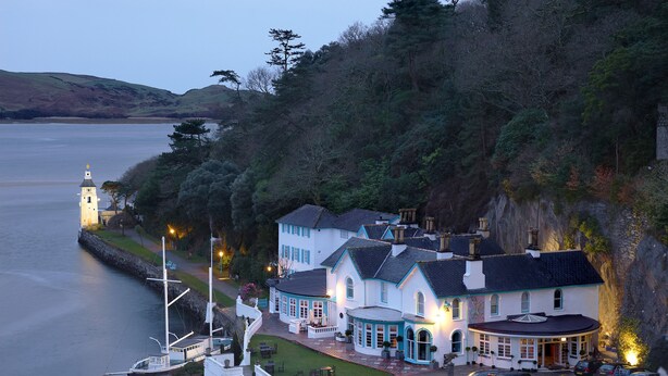 A coastal hotel with a lighthouse, multiple buildings, and a dock with boats.