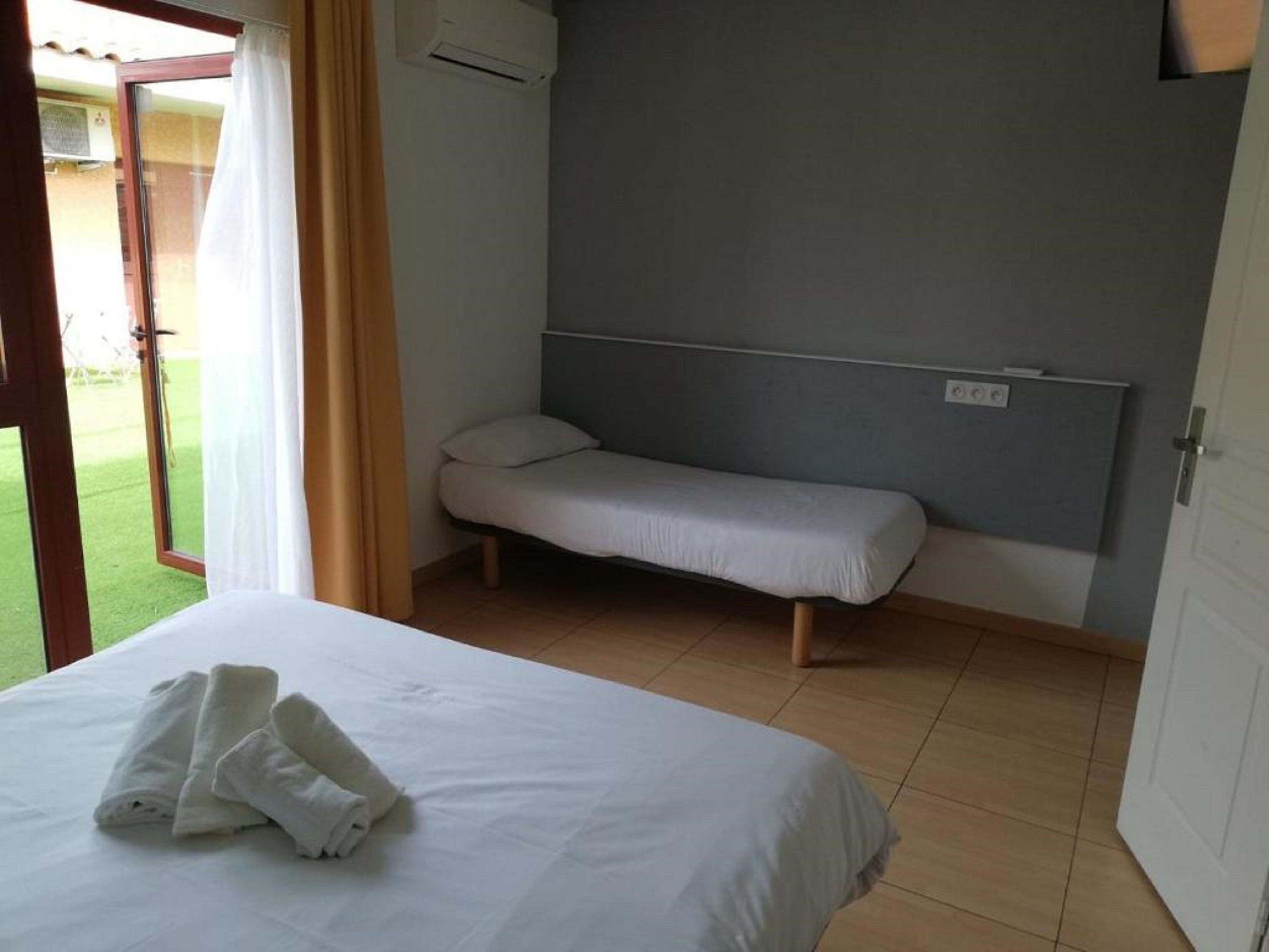 Un dormitorio con una cama, un banco, una puerta y una ventana con cortinas.