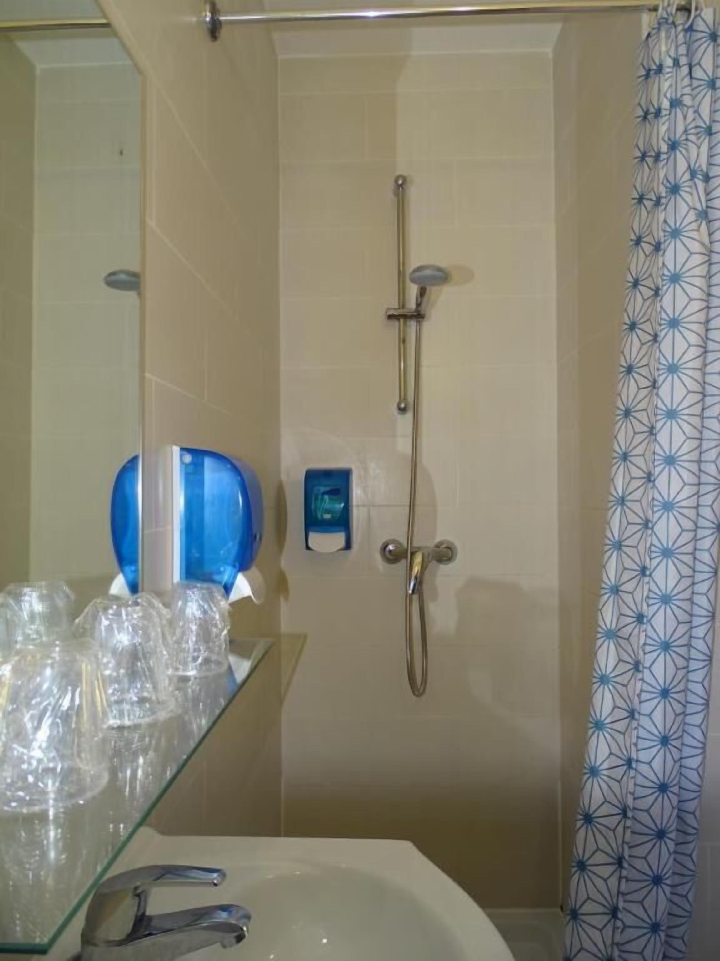 Un baño con repisas de vidrio para artículos de aseo, ducha con cabezal de ducha de mano y cortina de ducha estampada.