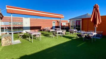 Un espace extérieur aménagé avec des tables et des chaises, une terrasse couverte et un bâtiment en arrière-plan.