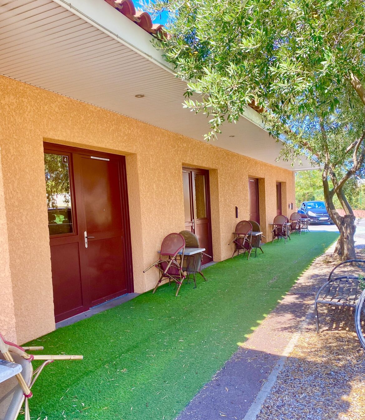 Una fila de habitaciones con un espacio al aire libre techado, cada una con una puerta y una silla.