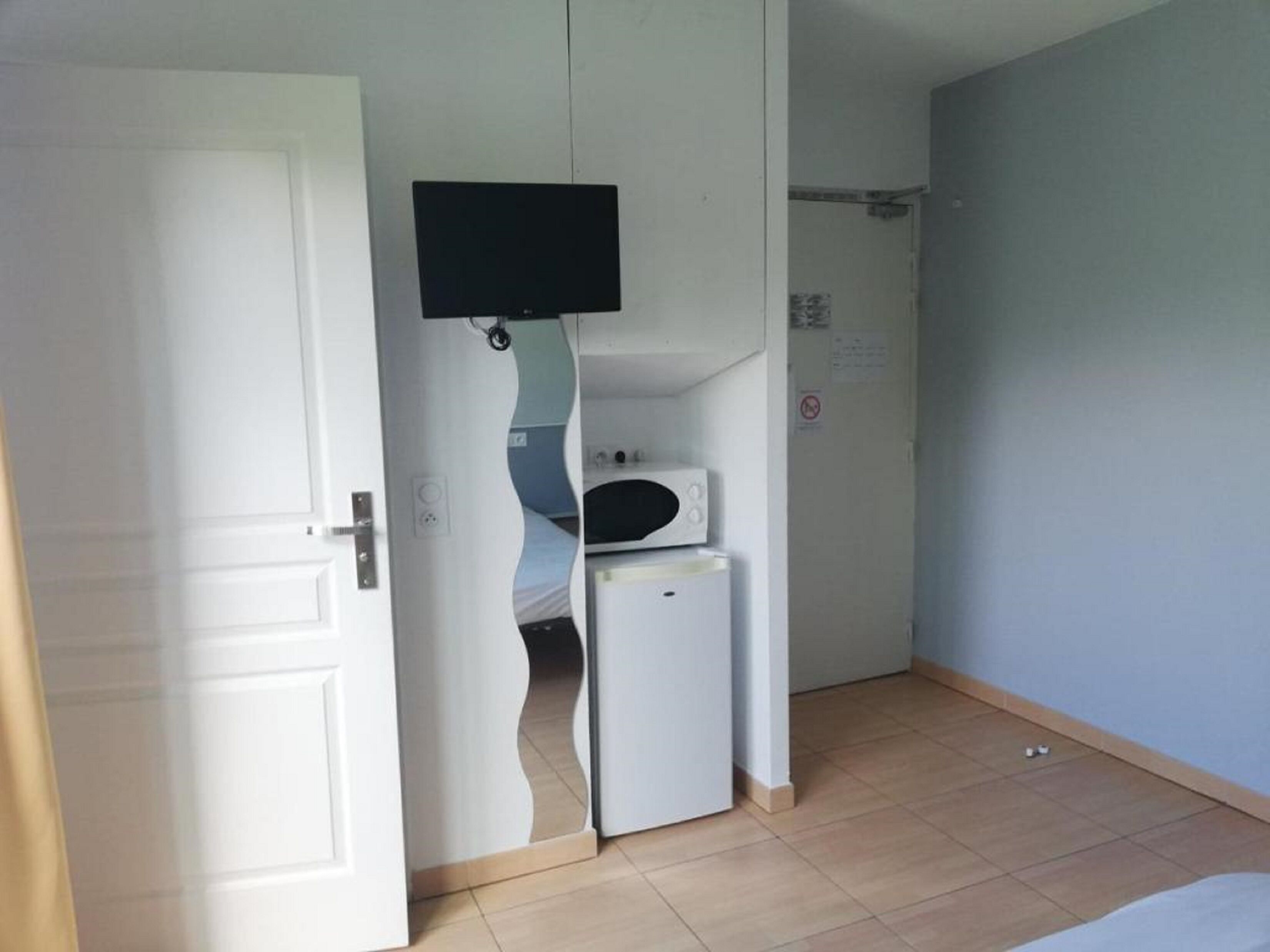 Una habitación pequeña con una cama, un microondas y un televisor fijado a la pared.