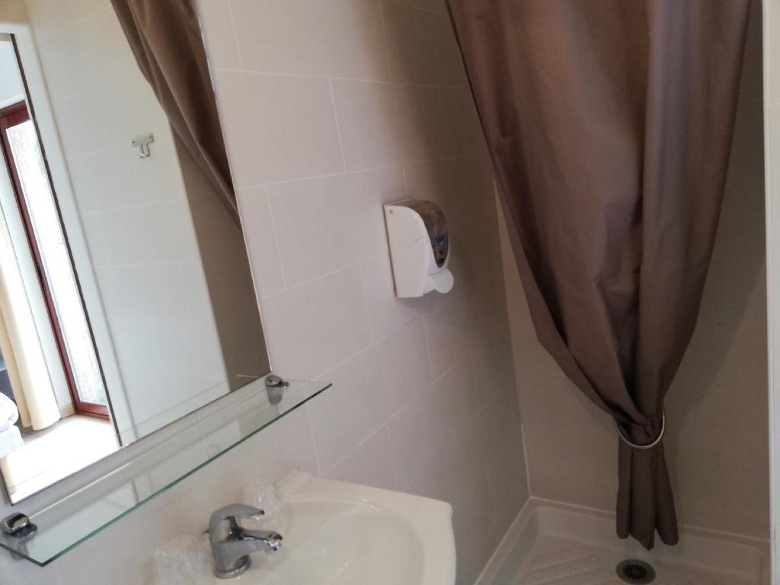 Une salle de bain avec une étagère en verre, un lavabo, un miroir, un distributeur de serviettes et un rideau de douche.