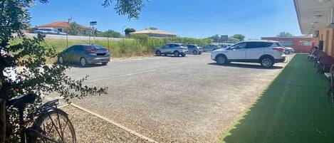 Un parking avec plusieurs voitures, un vélo et un bâtiment avec une pelouse verte au premier plan.