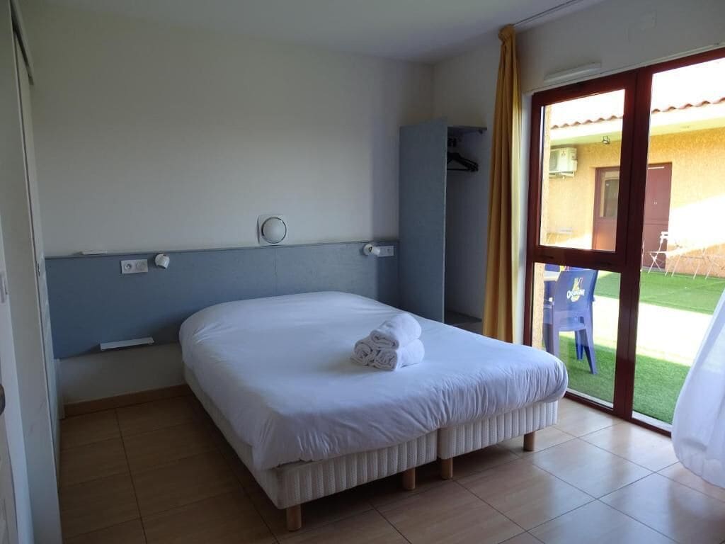 A hotel room with a bed, a window with curtains, a door, and a view of the outside.
