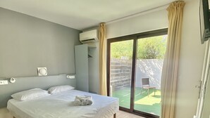A bedroom with a bed, a wardrobe, an air conditioning unit, and a sliding glass door leading to an outdoor area. - Hôtel Acajou (Argelès-sur-Mer)