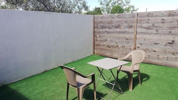 Un petit espace extérieur aménagé en patio, avec du gazon synthétique, deux chaises en plastique et une petite table.