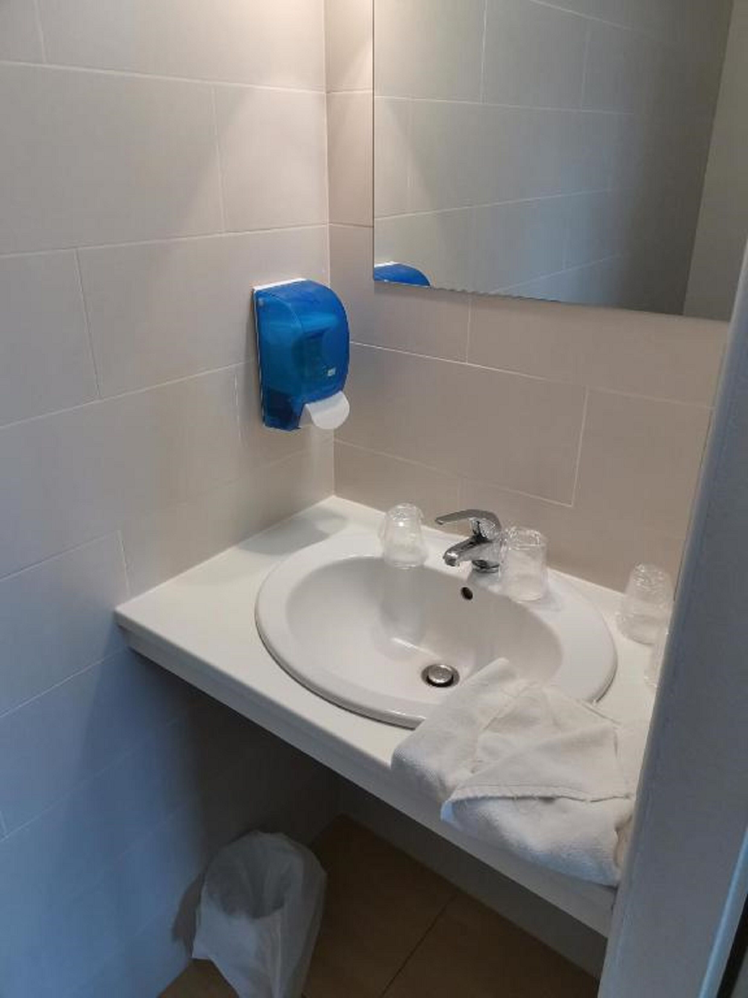 Un baño con un lavabo blanco, un espejo y un secamanos azul.