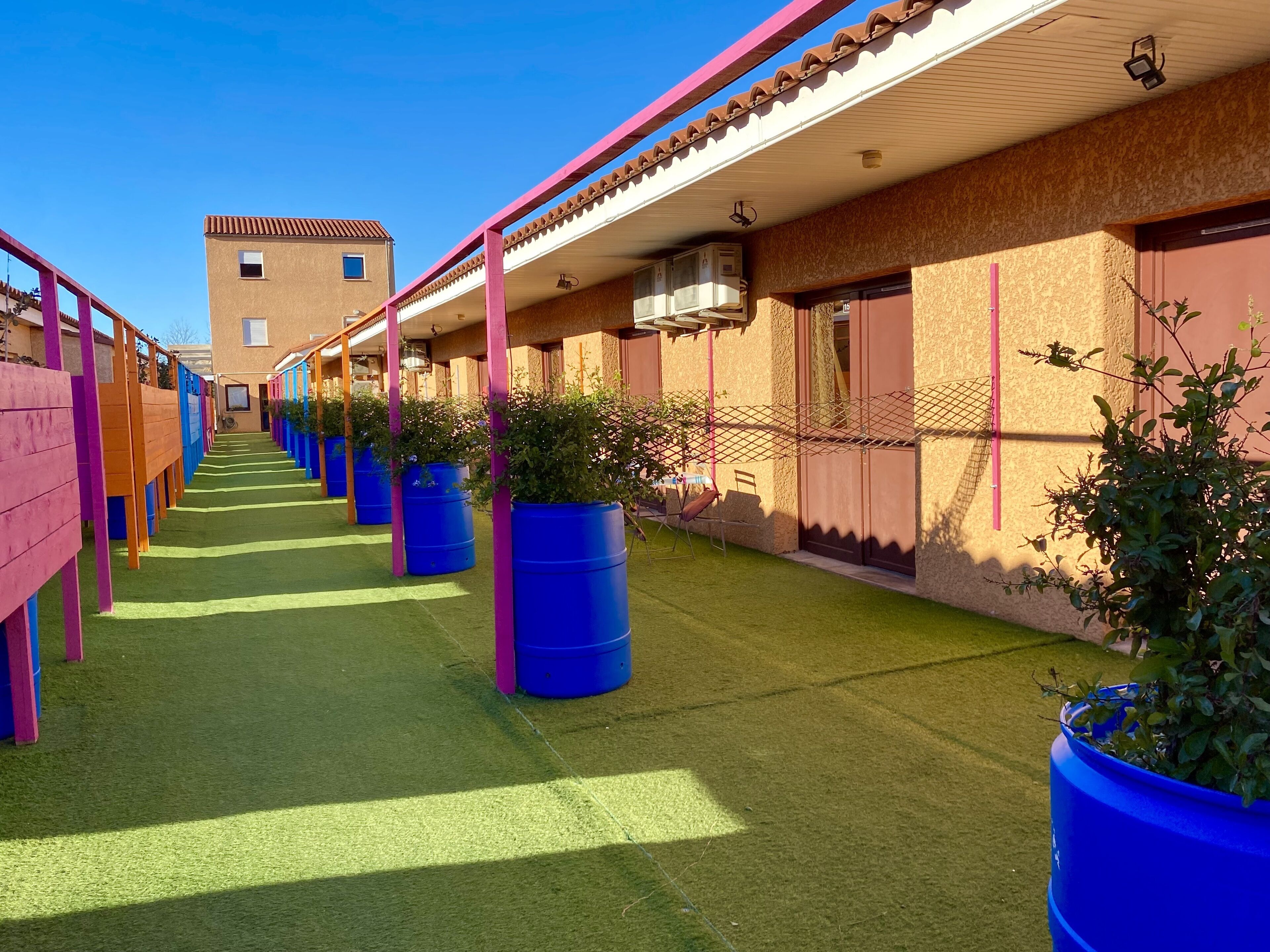 A row of hotel rooms with a central corridor, each room featuring a window, a door, and a balcony with a railing.