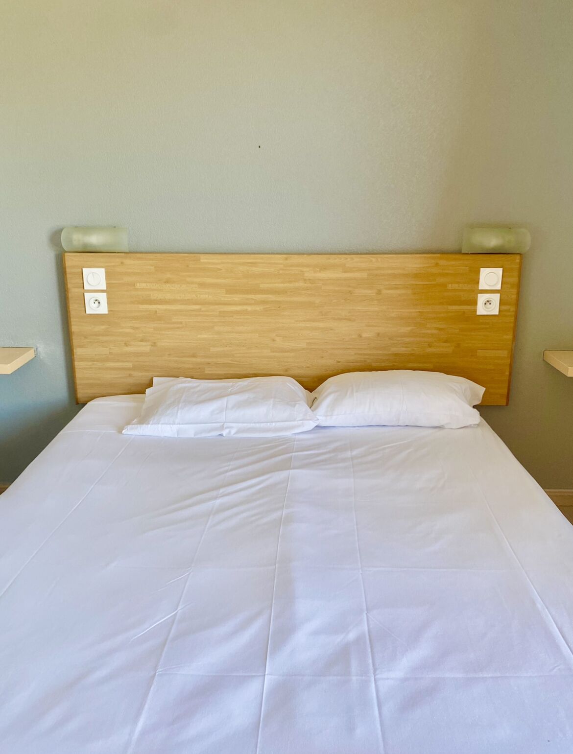A neatly made bed with white linens and a wooden headboard.