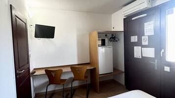 Een kleine hotelkamer met een bed, een bureau met twee stoelen, een kitchenette en een donkere deur met papieren.