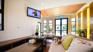 A modern living room with a sofa, a glass coffee table, a TV mounted on the wall, and a large window providing a view of the outdoors. - Ciao House (Hengchun)