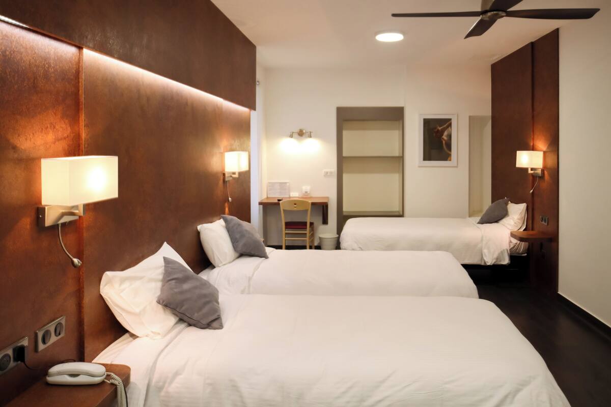 Una habitación de hotel con dos camas, un escritorio, una silla y un ventilador de techo.