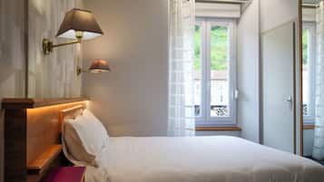Un dormitorio con cama, mesita de noche, lámpara, ventana con cortinas y puerta.
