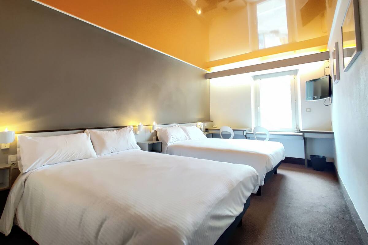 Habitación de hotel con dos camas, un escritorio, sillas, un televisor y una ventana.