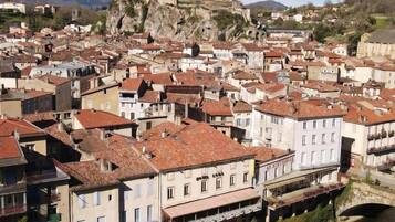 A historic town with a prominent castle on a hill, surrounded by densely packed buildings with red-tiled roofs, a river, and a bridge.