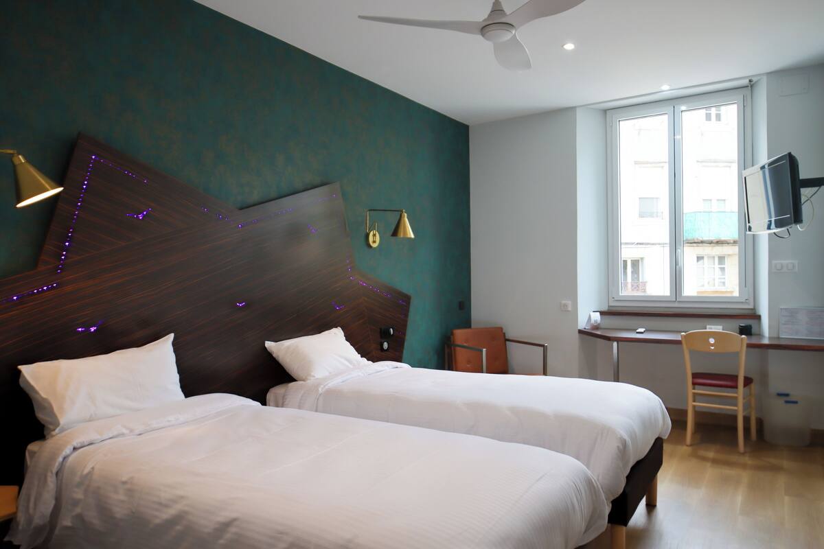 Una habitación de hotel con dos camas, un escritorio, una silla, un televisor y un ventilador de techo.