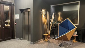 Un hall d’entrée moderne avec un mur foncé, une porte en bois et une sculpture géométrique bleue.