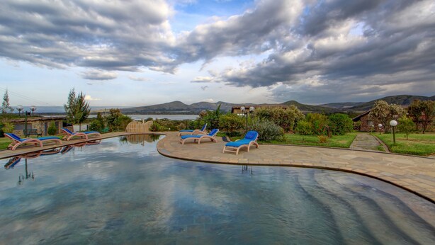 Une piscine entourée de chaises longues, elle-même bordée d’un jardin aménagé et offrant une vue sur des collines lointaines.