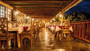 Un restaurant avec des tables et des chaises en bois, recouvertes de nappes blanches et de serviettes rouges, sous un toit en bois.