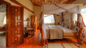 Une pièce avec un plafond en bois, un lit à baldaquin, une porte en bois ornée d’une fleur et une fenêtre avec des rideaux.