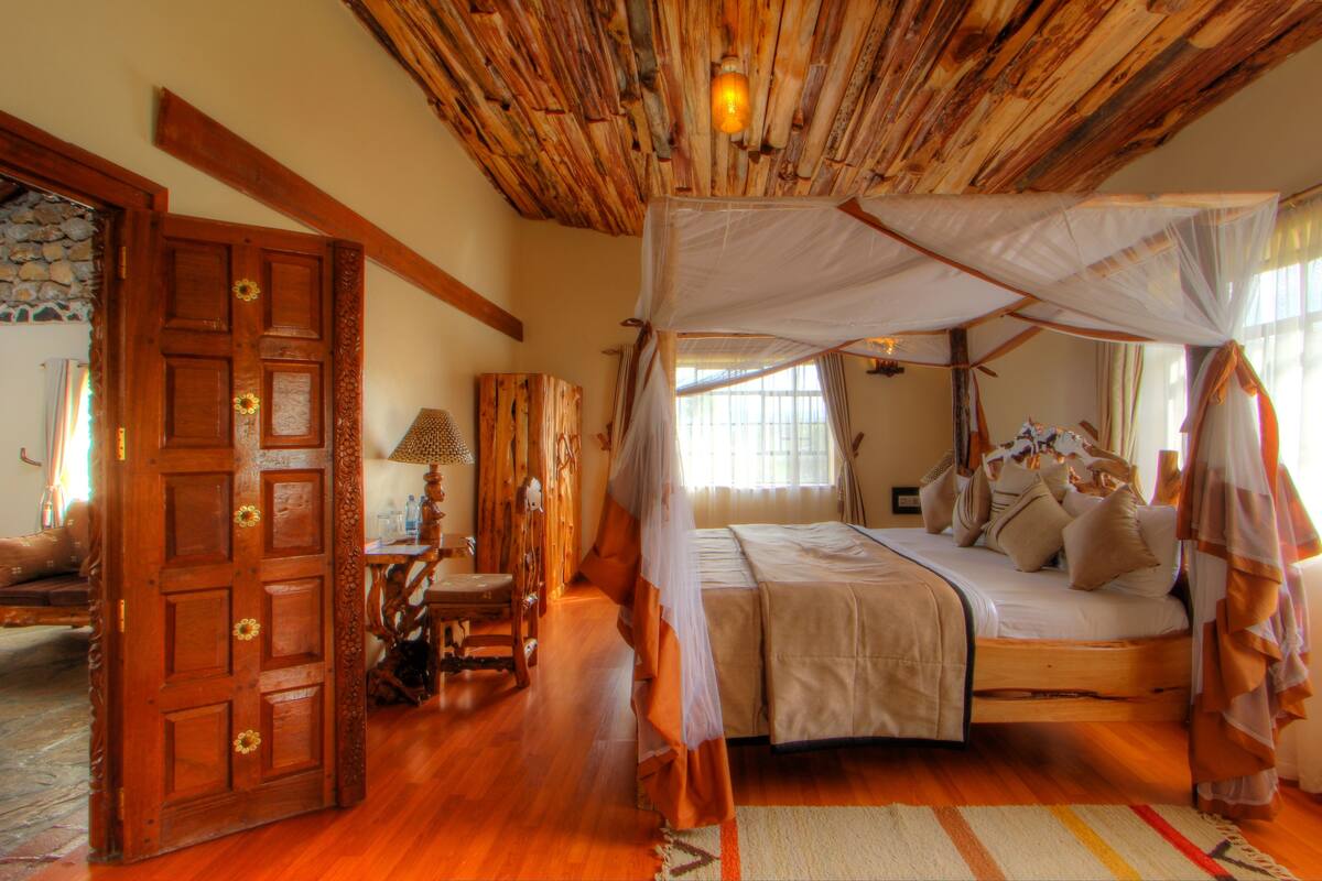 Une pièce avec un plafond en bois, un lit à baldaquin, une porte en bois ornée d’une fleur et une fenêtre avec des rideaux.