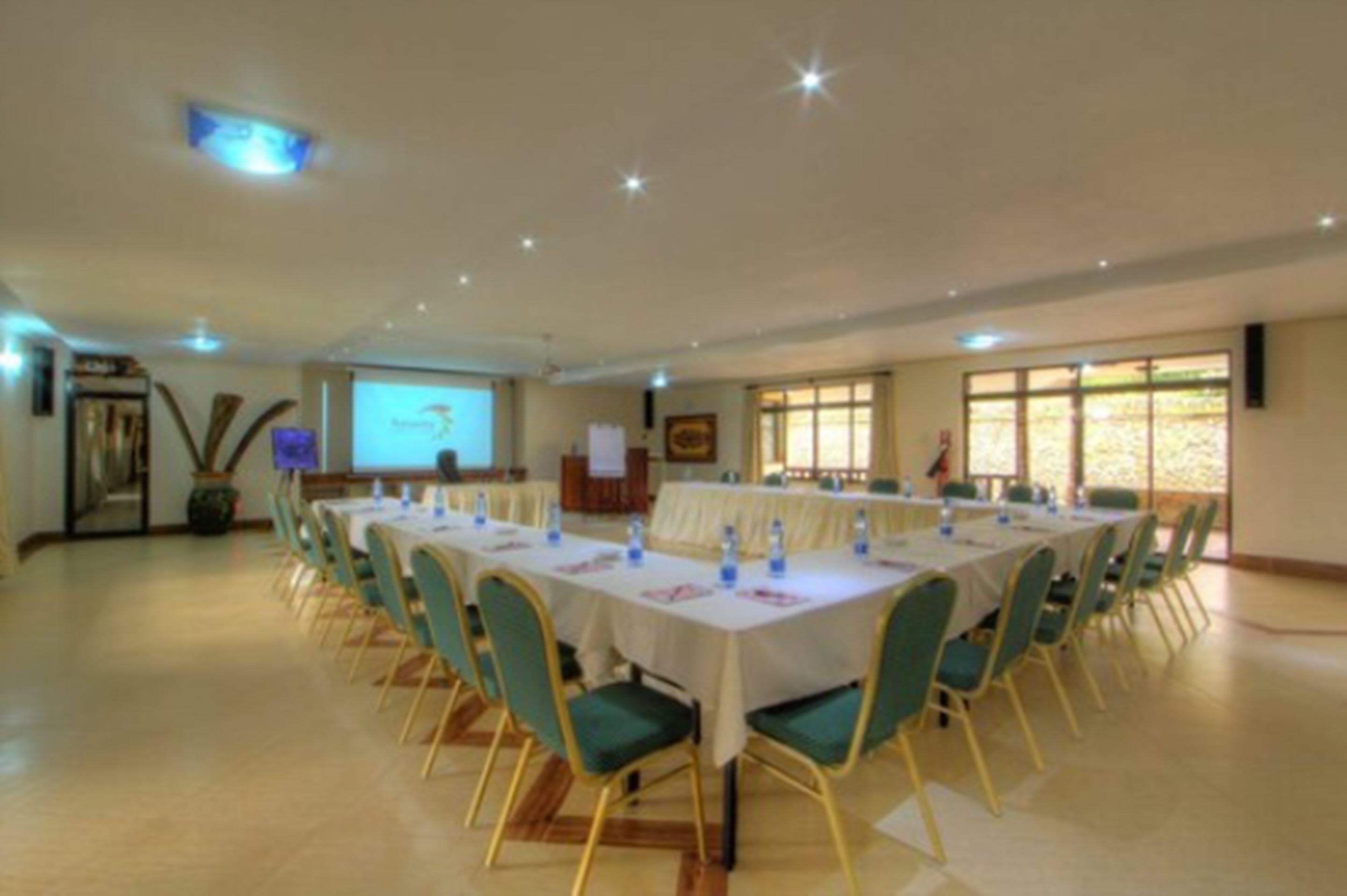 A conference room with multiple tables and chairs, a projector screen, and a presentation area.