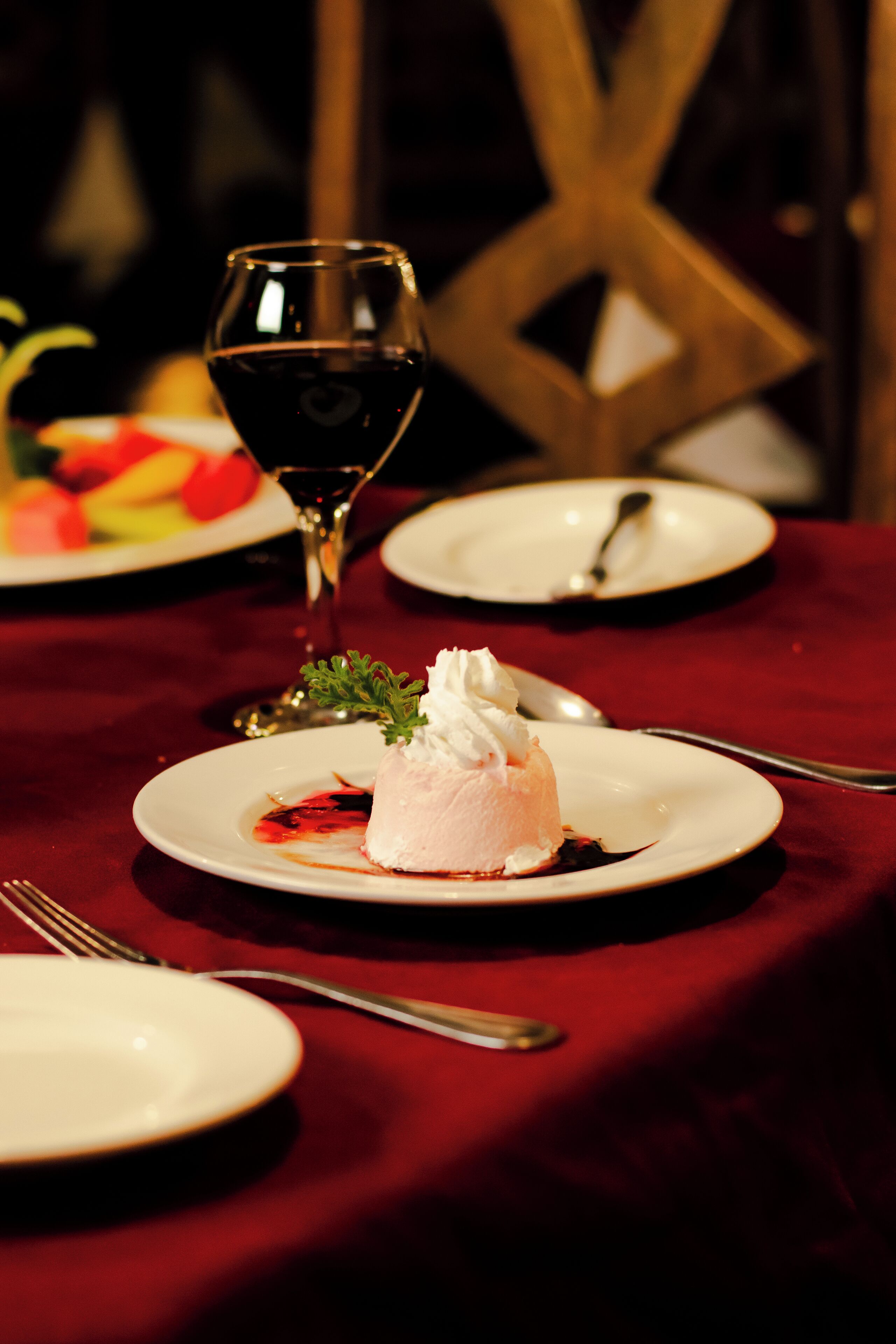Un plato de postre con una porción de helado y una copa de vino tinto sobre una mesa con mantel rojo.