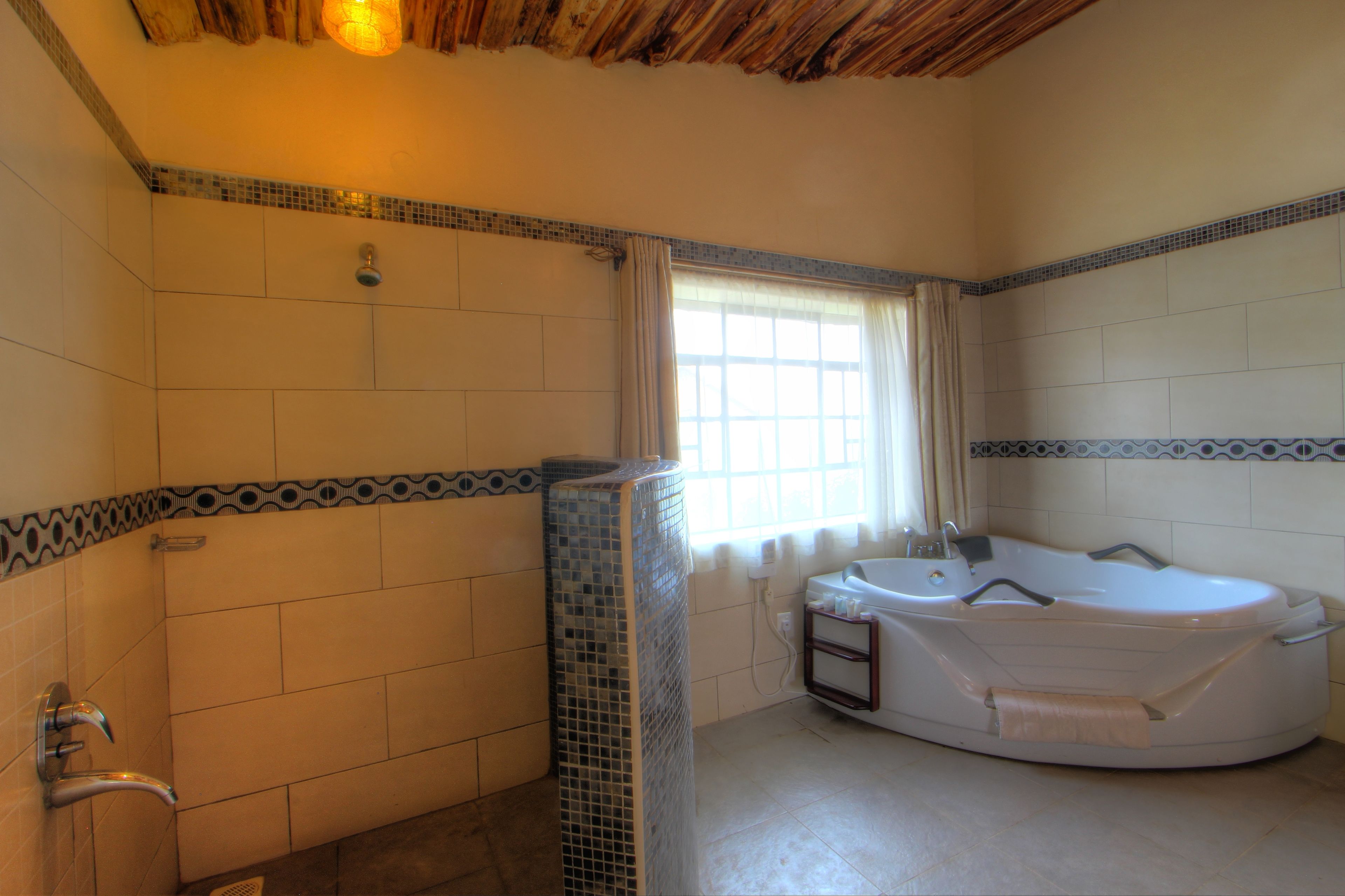Een badkamer met een groot bad, betegelde wanden en een raam met gordijnen.