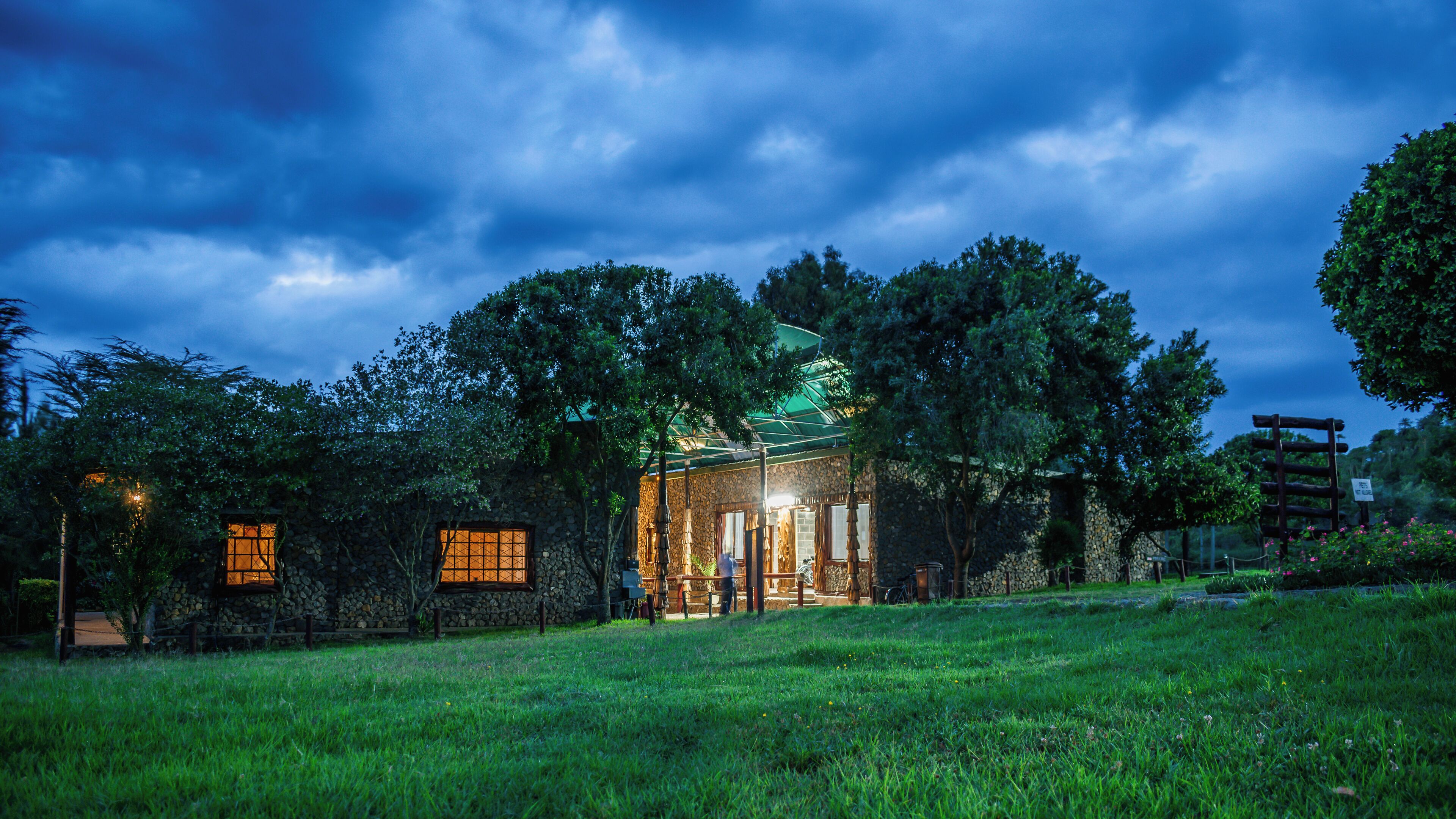 A rustic stone building with a green roof, surrounded by lush greenery and trees.