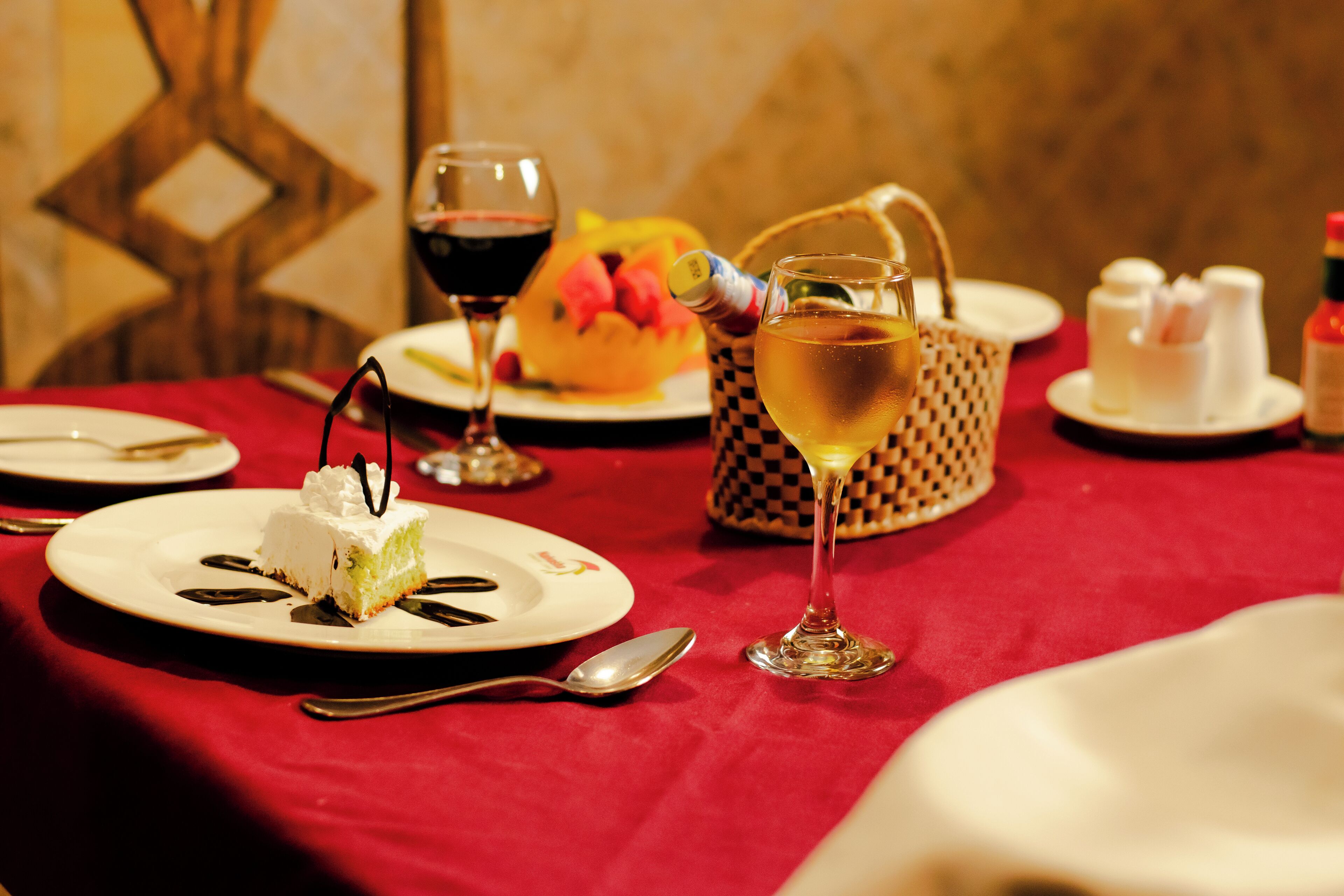 A dining table with plates of food, glasses of wine, and a basket.