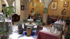 A dining area with tables, chairs, potted plants, and a central fountain. - Hotel Riad Benatar (Essaouira)
