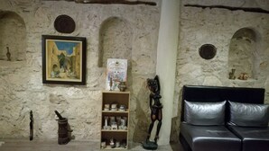 A room with a stone wall, a framed painting, a shelf with jars, a sculpture, and a leather sofa. - Hotel Riad Benatar (Essaouira)