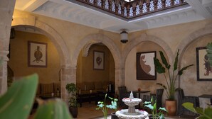 An interior courtyard with arches, potted plants, a fountain, and artwork on the walls. - Hotel Riad Benatar (Essaouira)